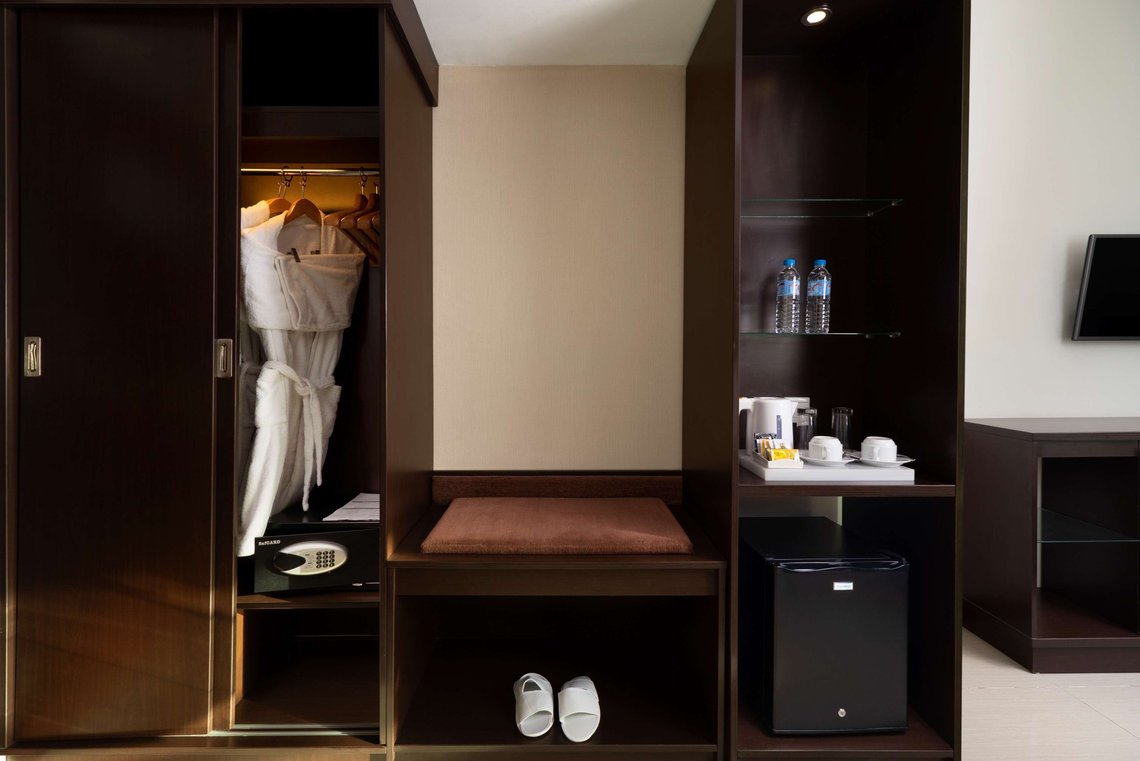 Een hotelkamer met een kledingkast, zithoek, minibar en een plank met toiletartikelen.