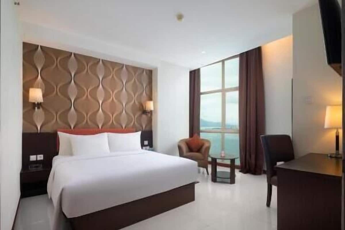 A hotel room with a bed, a desk, a chair, a small table, and a view of the outdoors.
