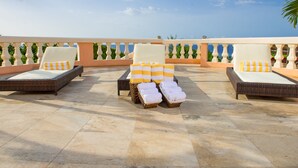 Una terraza en la azotea con sillones de mimbre y cojines, suelo de baldosas y barandilla decorativa.