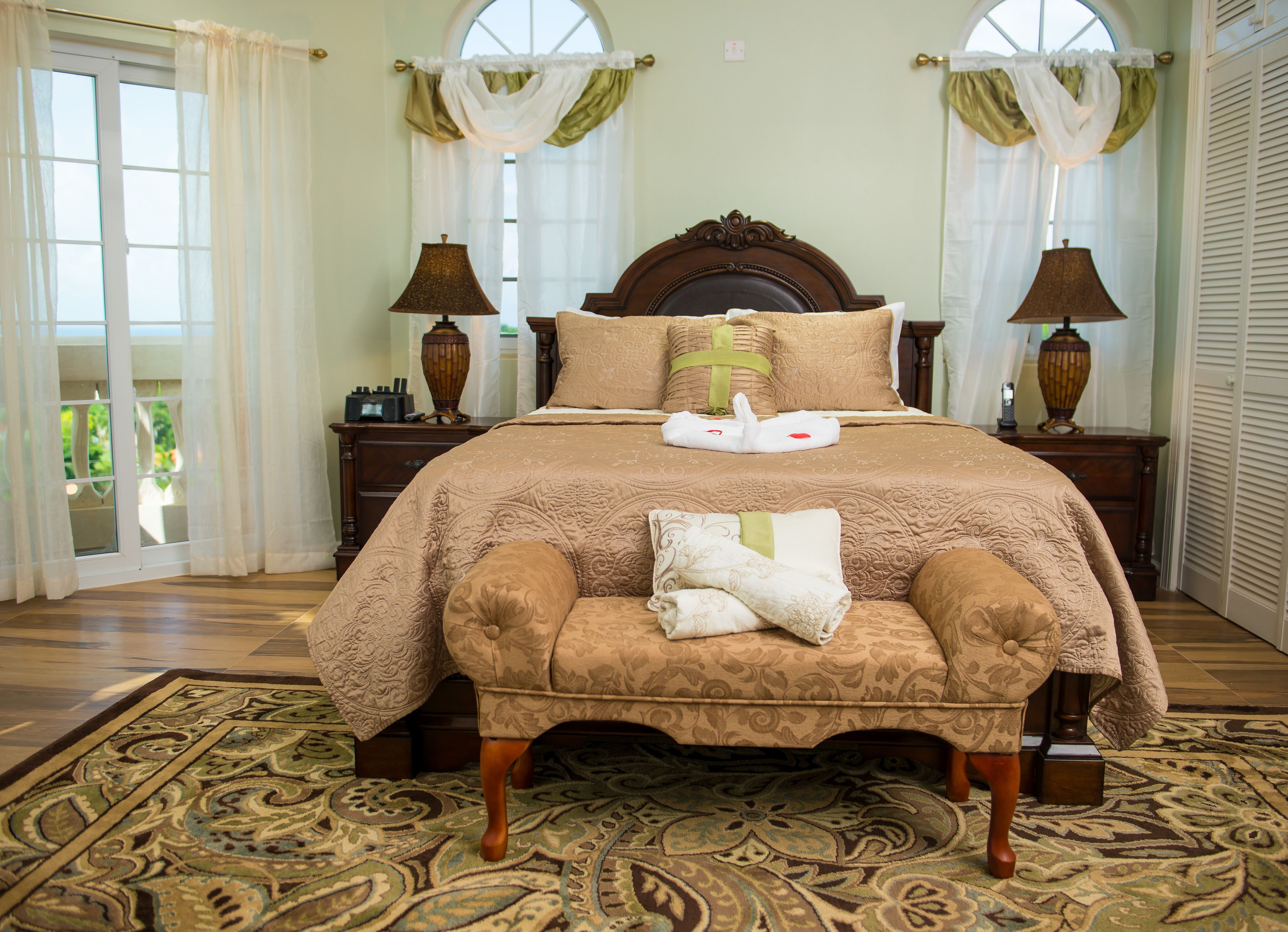 A spacious bedroom with a large bed, two nightstands, a wooden headboard, and a matching armchair.