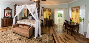 A four-poster canopy bed with a nightstand, a chaise lounge, a desk with a chair, and a large mirror.