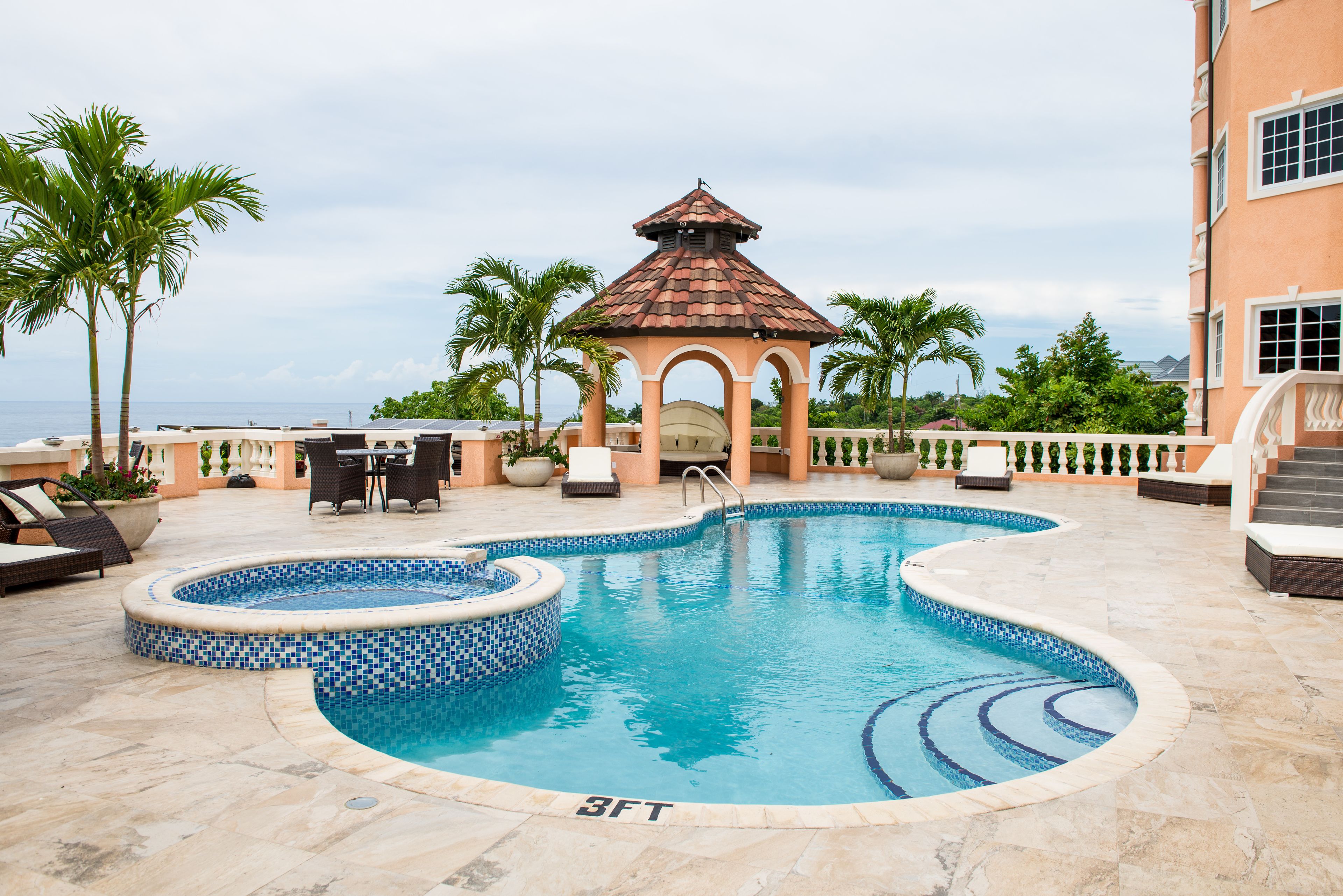 A swimming pool with a gazebo, palm trees, and a view of the ocean.