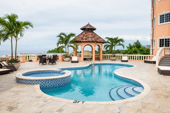 A swimming pool with a gazebo, palm trees, and a view of the ocean.