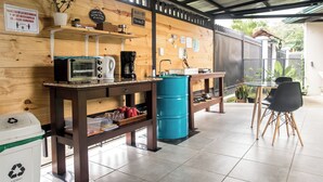 A café with wooden walls, a coffee machine, a blue barrel, and a table with chairs. - Terida Airport B&B (Desamparados)