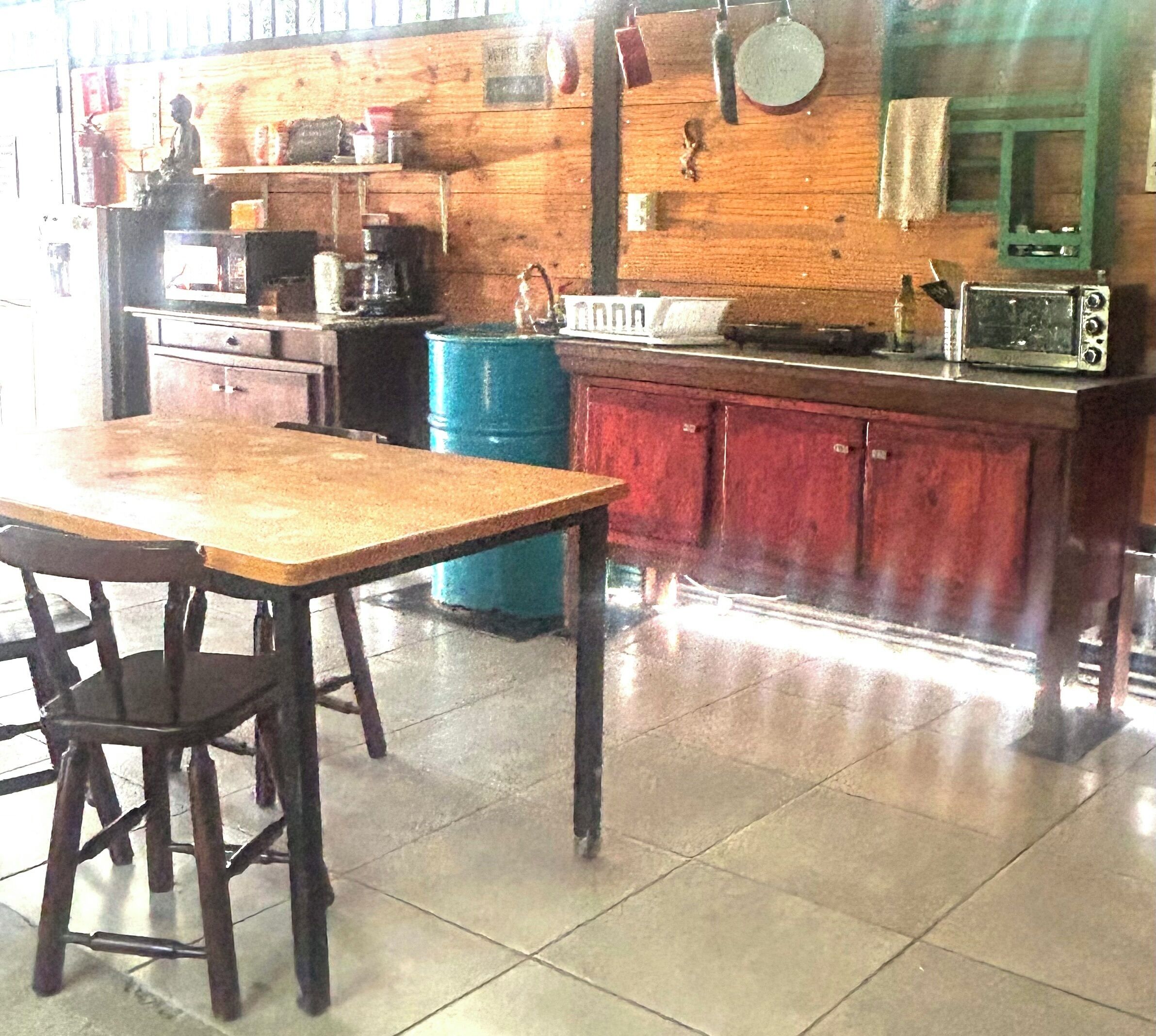 Una cocina con una mesa de madera, sillas, un barril azul y un armario rojo.