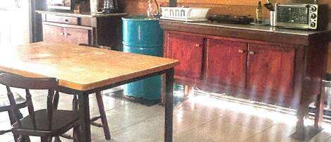 Una cocina con una mesa de madera, sillas, un barril azul y un armario rojo.
