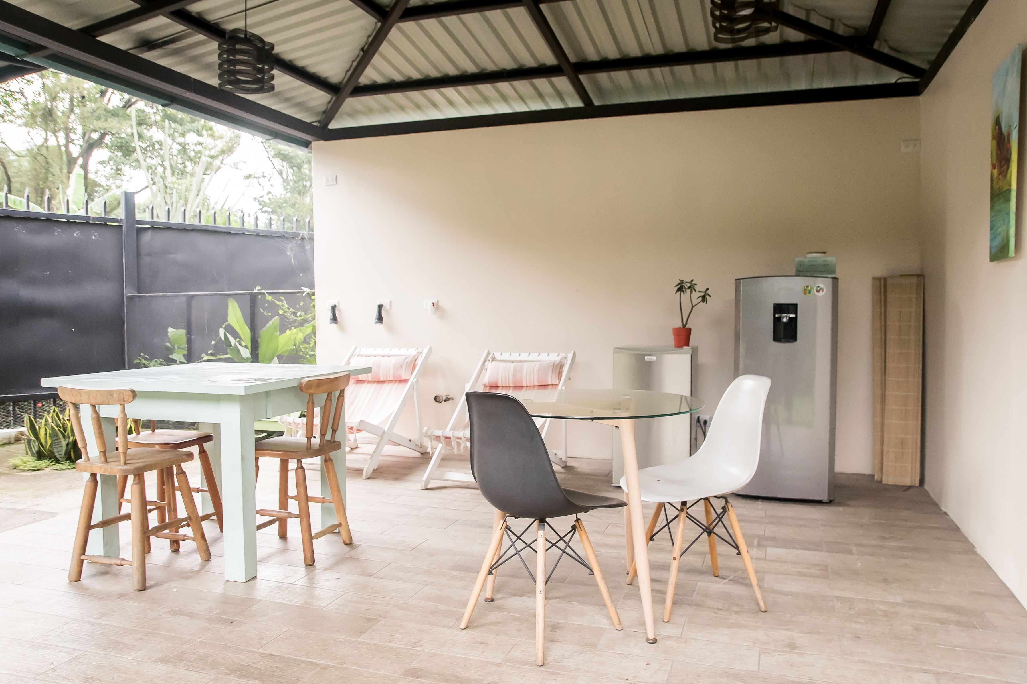 Un espace extérieur abrité, aménagé pour prendre les repas, avec une table et des chaises, un réfrigérateur et une plante en pot.