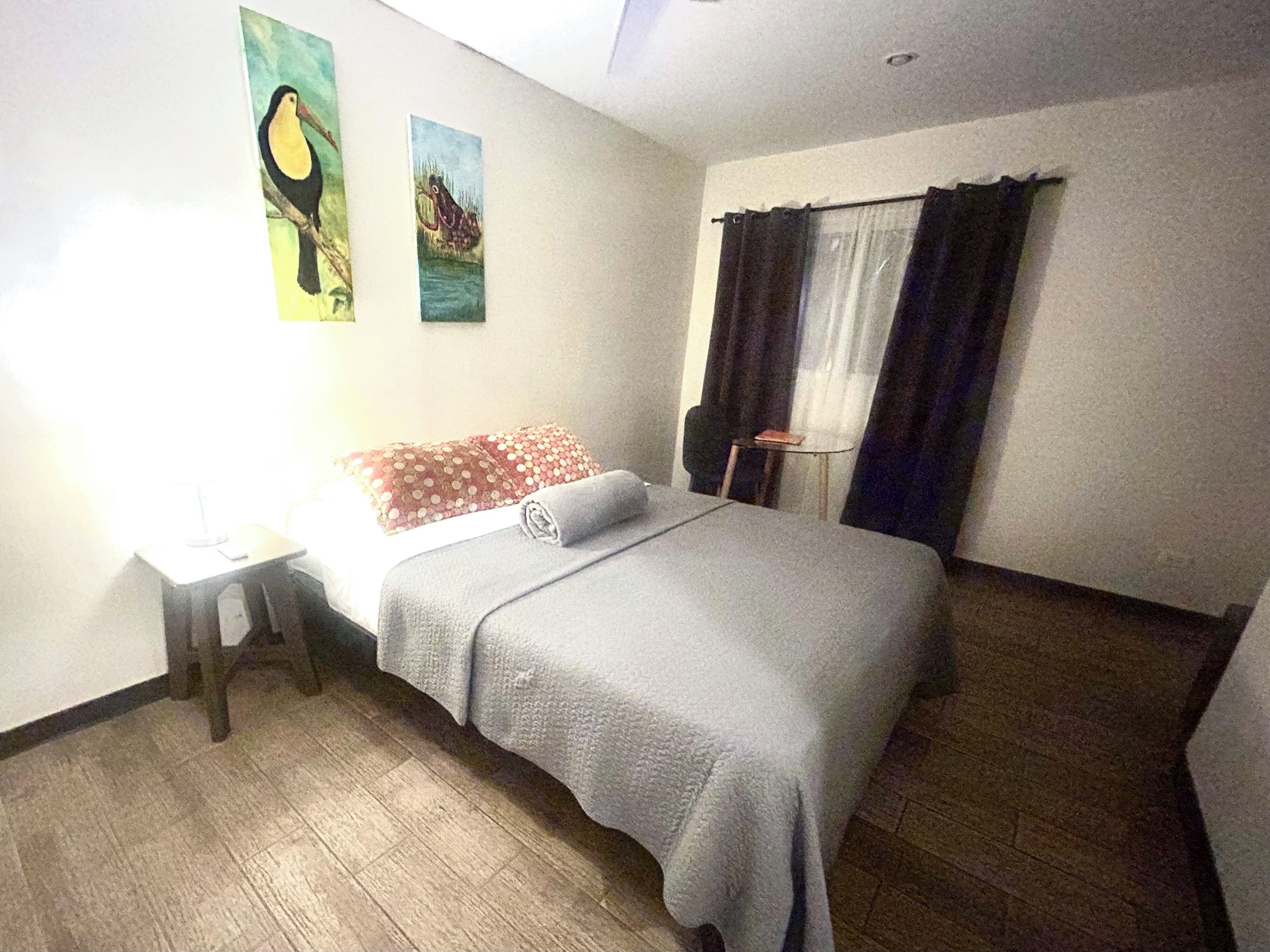 Una habitación de hotel con una cama, una mesita, una lámpara y dos cuadros en la pared.