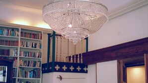 Une pièce avec un grand lustre, une bibliothèque, un escalier en bois, une lampe et un lit.