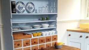 Une cuisine avec un meuble bleu, des tiroirs en bois et un tabouret rouge.