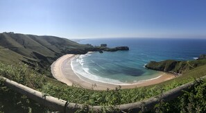 A coastal landscape with a curved sandy beach, green hills, and the ocean. - El Rincon del Cuera (Llanes)