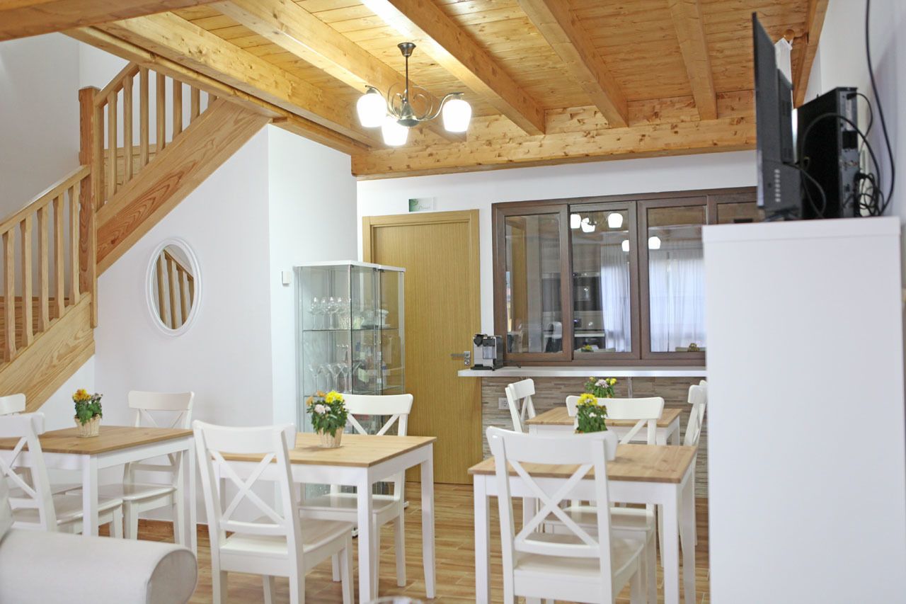 A dining area with white chairs and wooden tables, a staircase with wooden railings, and a kitchen area with a refrigerator and a microwave.
