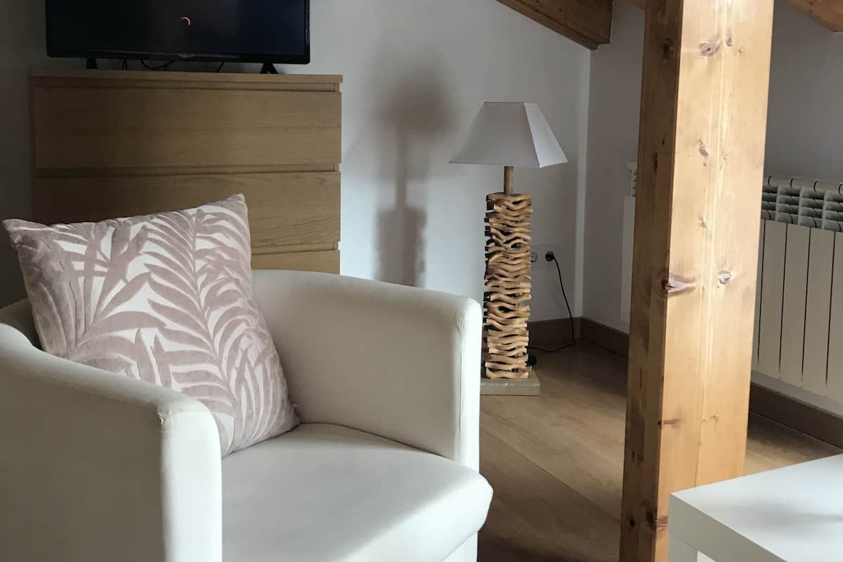 A living room with a white sofa, a television displaying 'NETFLIX', and a wooden ceiling structure.