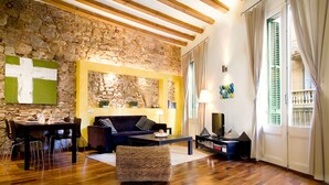 Un salon avec un mur en pierre, un plancher en bois, un canapé, une table basse et un téléviseur.