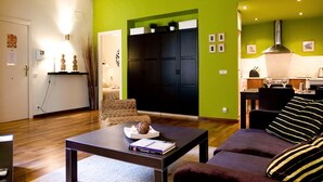 Un salon avec un plancher en bois, un canapé, une table basse et un coin cuisine équipé d’une cuisinière et de placards.