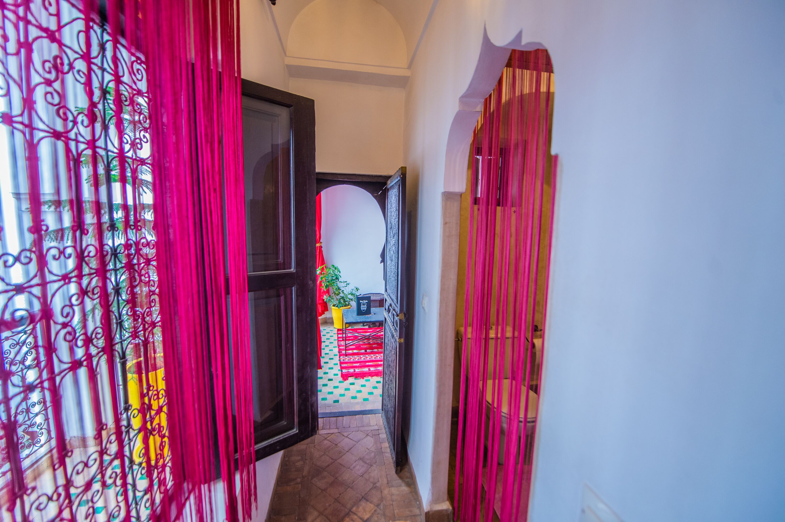 A hallway with a view into a room featuring a tiled floor and a potted plant.