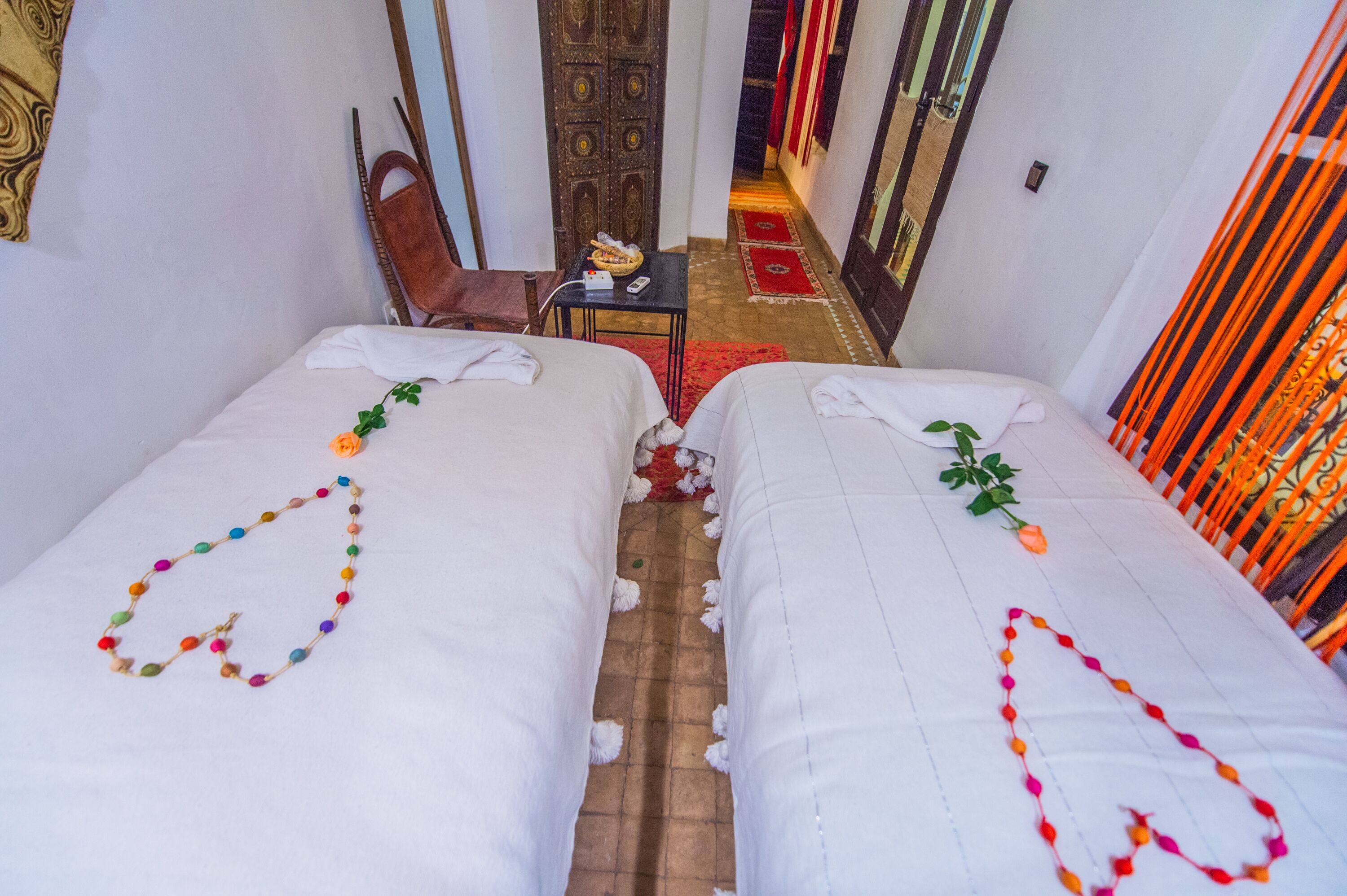 Hotelkamer met twee bedden, een klein tafeltje met een schaal en een afstandsbediening, en een rood tapijt dat naar een deur leidt.