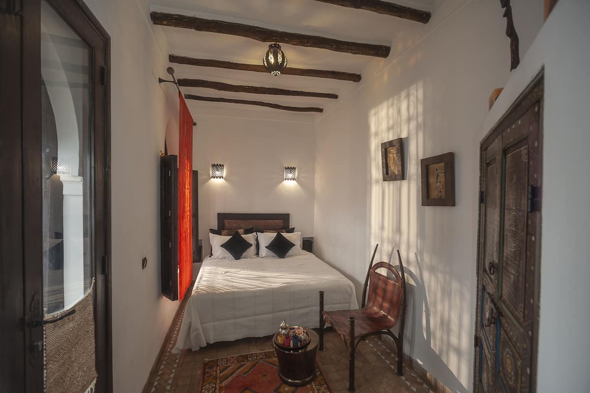 A narrow hallway leading to a bedroom with a bed, a chair, and a decorative wall.