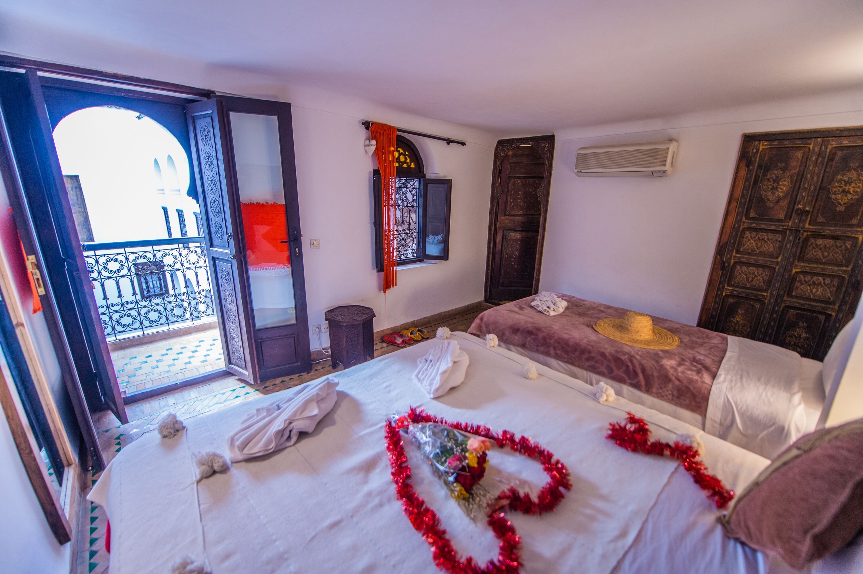 A hotel room with two beds, a balcony, a decorative curtain, and a traditional wooden door.