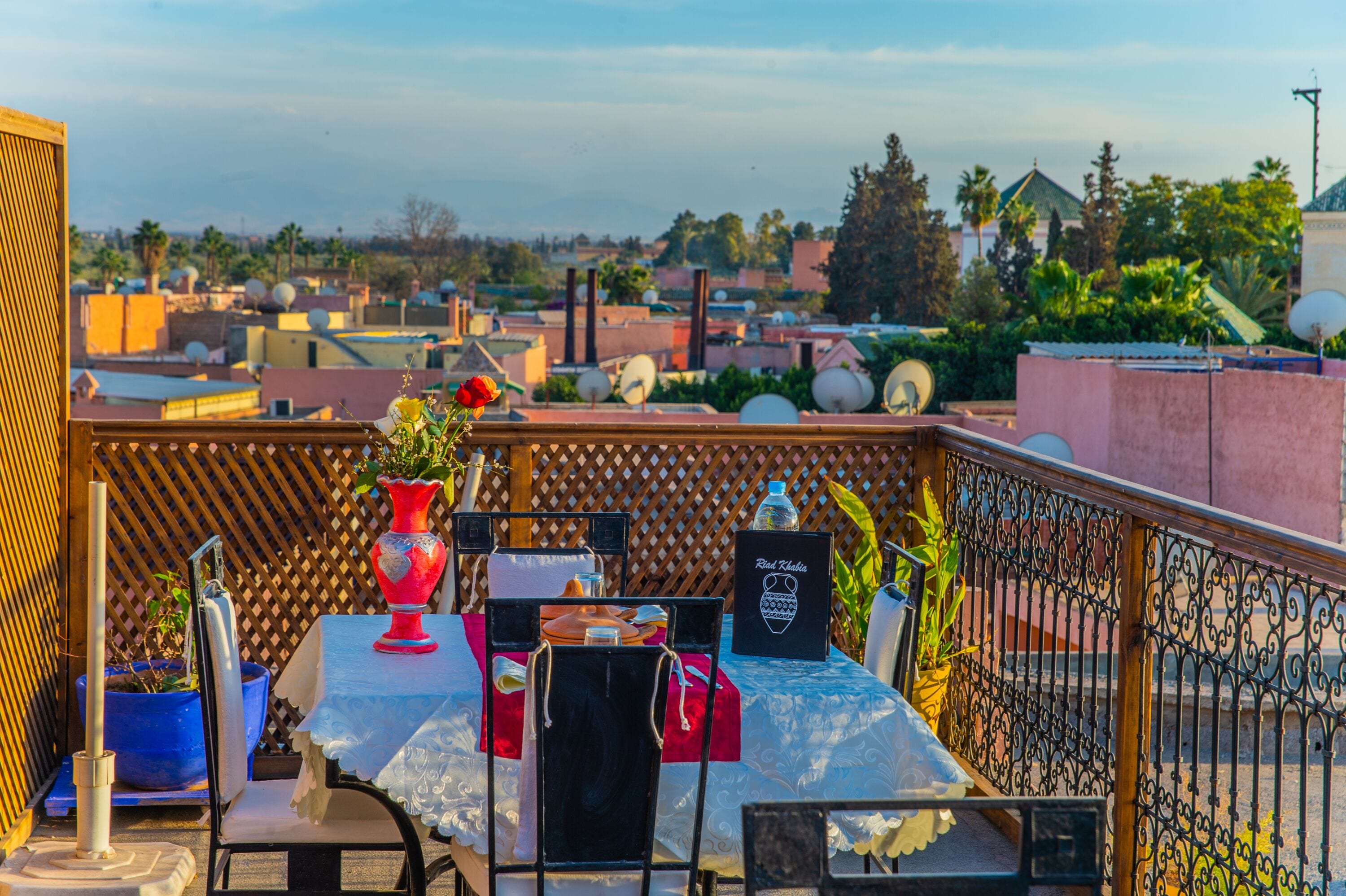 Terraza en la azotea con una mesa lista para comer, rodeada por una valla decorativa y plantas en macetas.