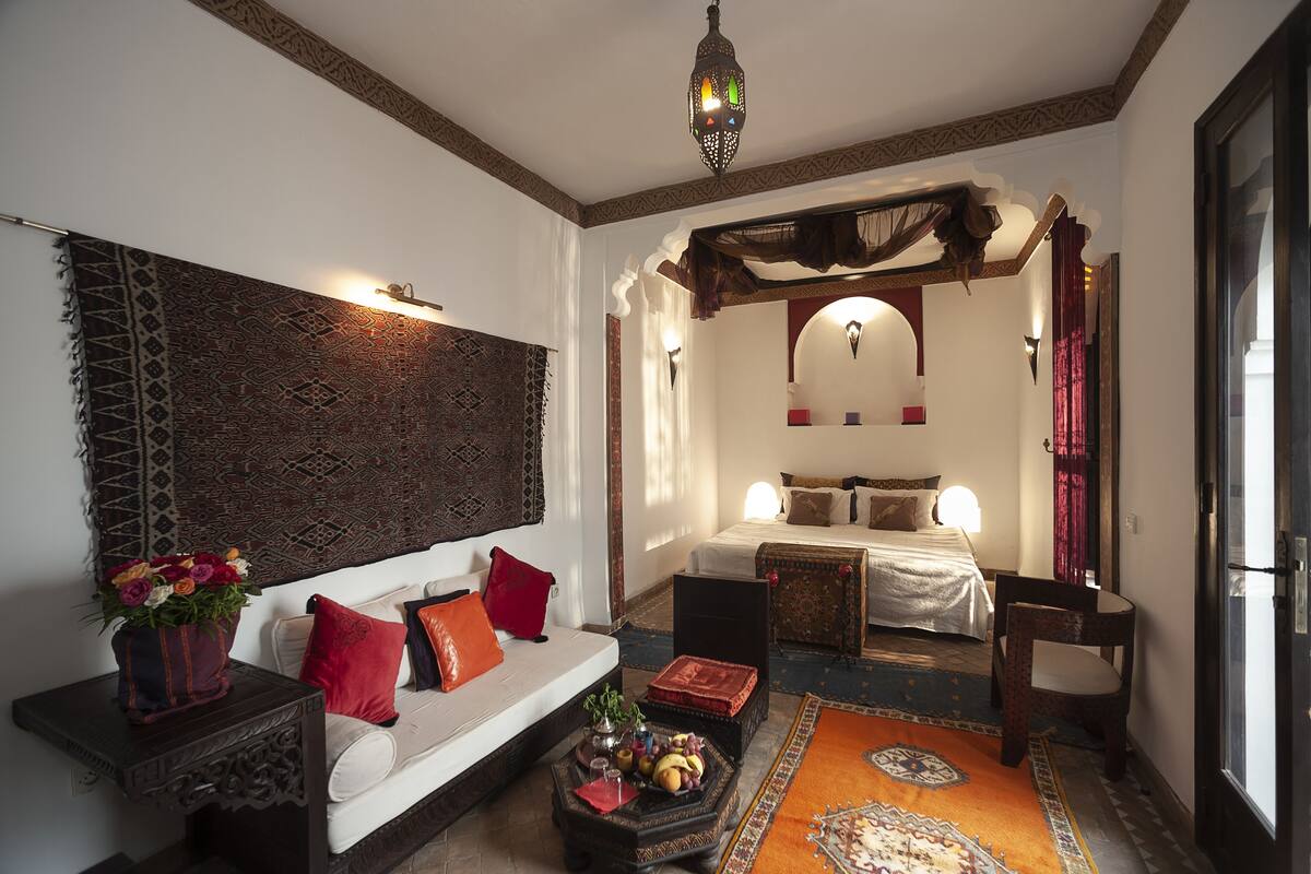 A traditional room with a sofa, a bed, a coffee table with fruits, and a decorative wall hanging.