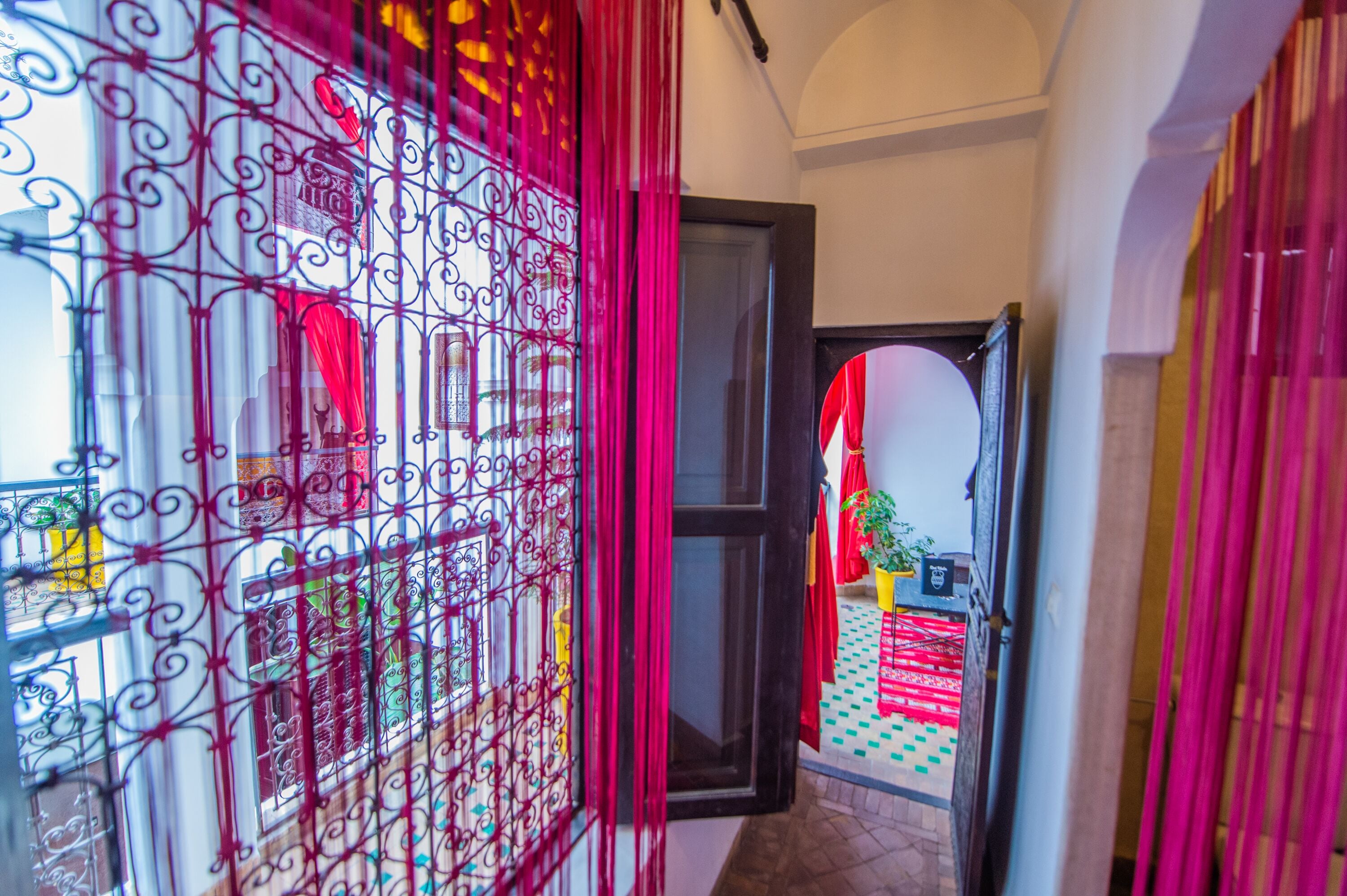 A hallway with a metal gate, a door, and a view of a balcony with red curtains.
