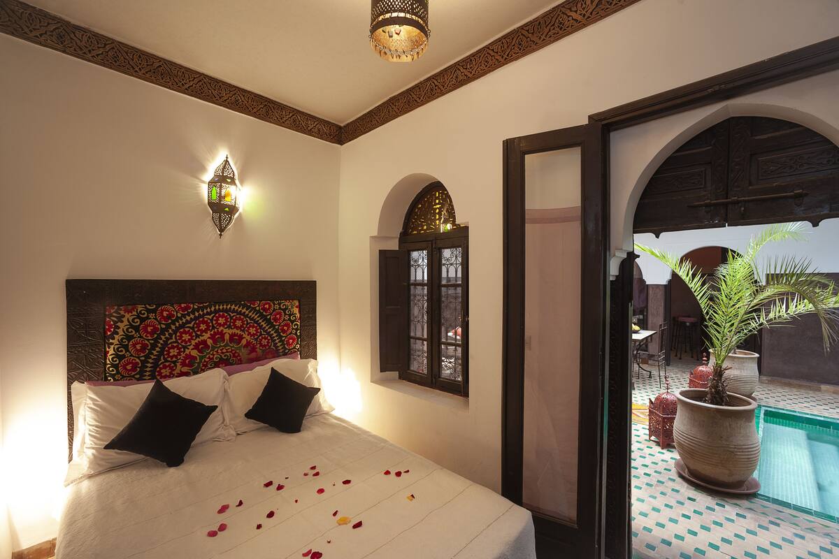 A bedroom with a bed, a wall-mounted light, and a view of a swimming pool.