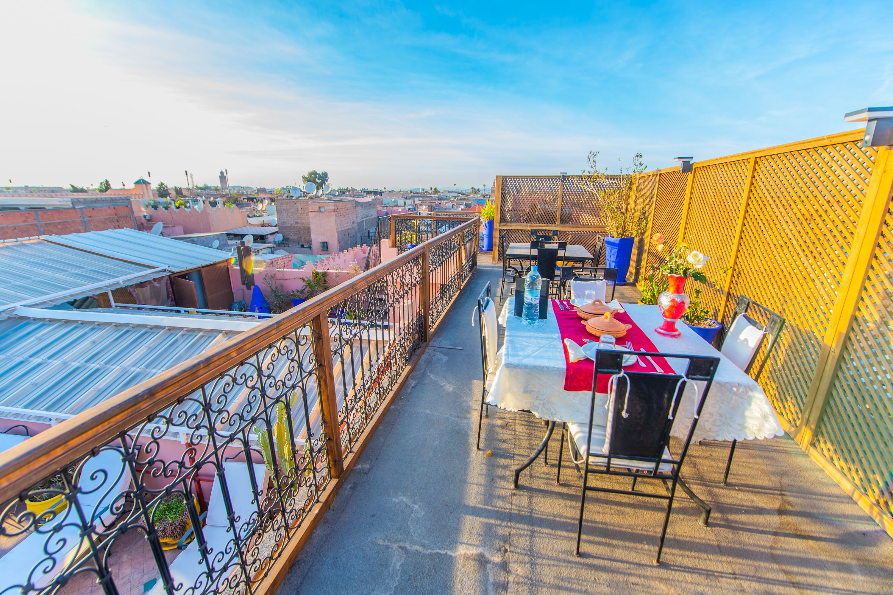 A rooftop terrace with a table set for dining, surrounded by a yellow fence and metal railing.
