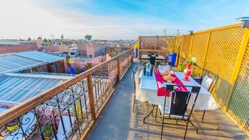 A rooftop terrace with a table set for dining, surrounded by a yellow fence and metal railing.