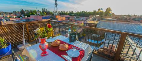A rooftop terrace with a table set for dining, potted plants, and a view of the surrounding buildings.