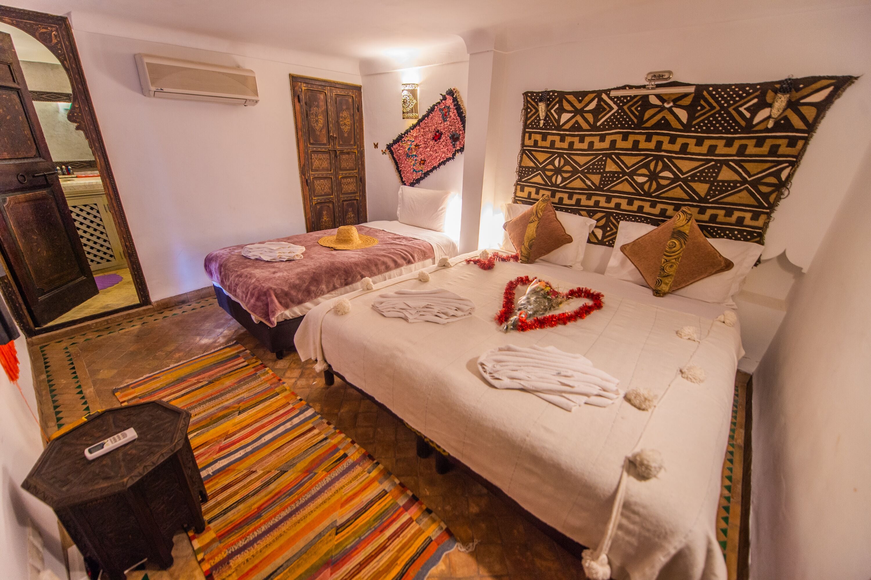 A hotel room with two beds, a colorful striped rug, a wooden door, and a patterned tapestry on the wall.