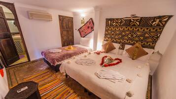 A hotel room with two beds, a colorful striped rug, a wooden door, and a patterned tapestry on the wall.