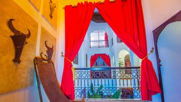 Un intérieur traditionnel avec des rideaux rouges, un fauteuil suspendu et un balcon doté d’une rambarde en métal.