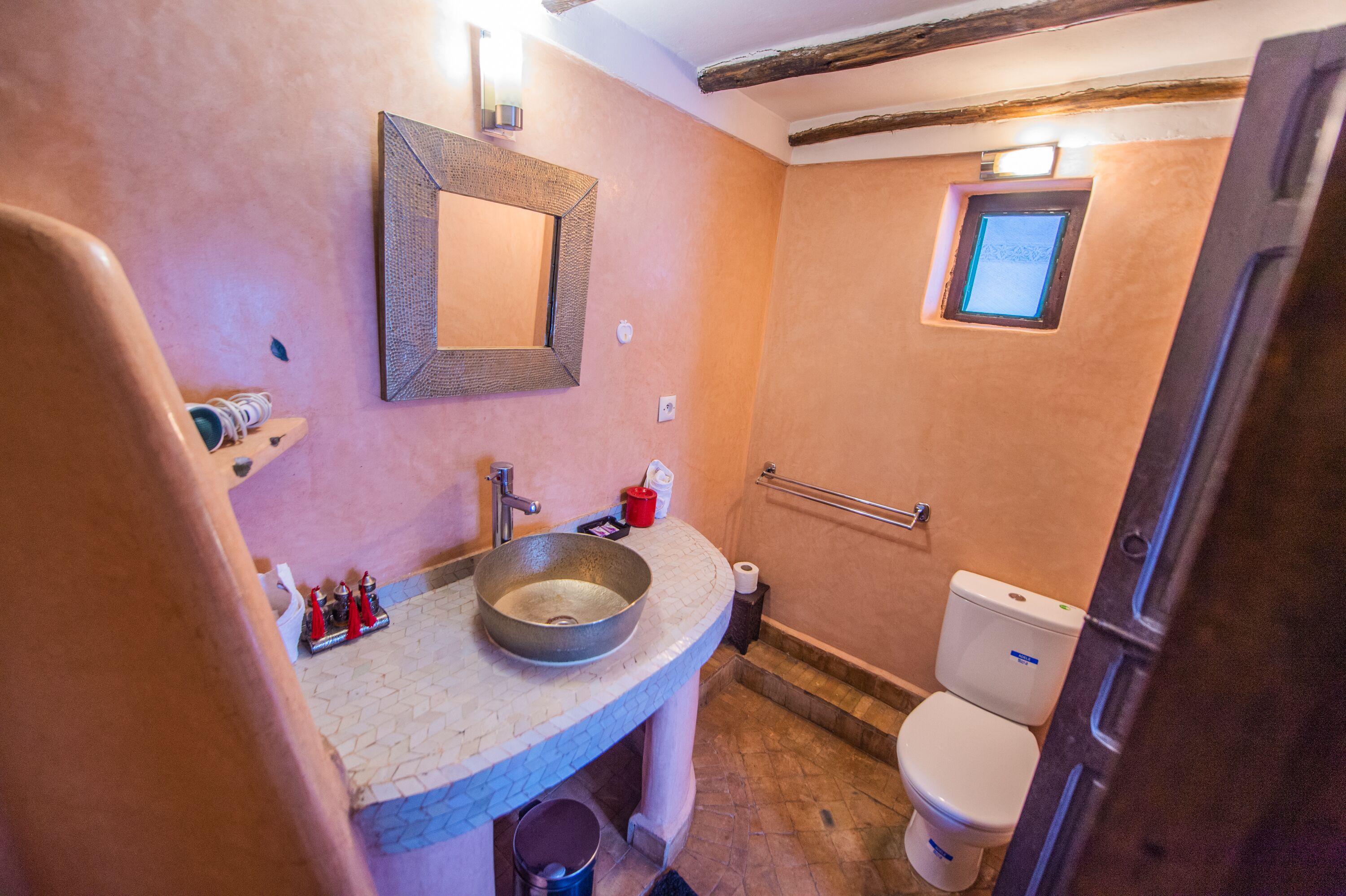 A bathroom with a stone sink, a mirror, a toilet, and a small window.