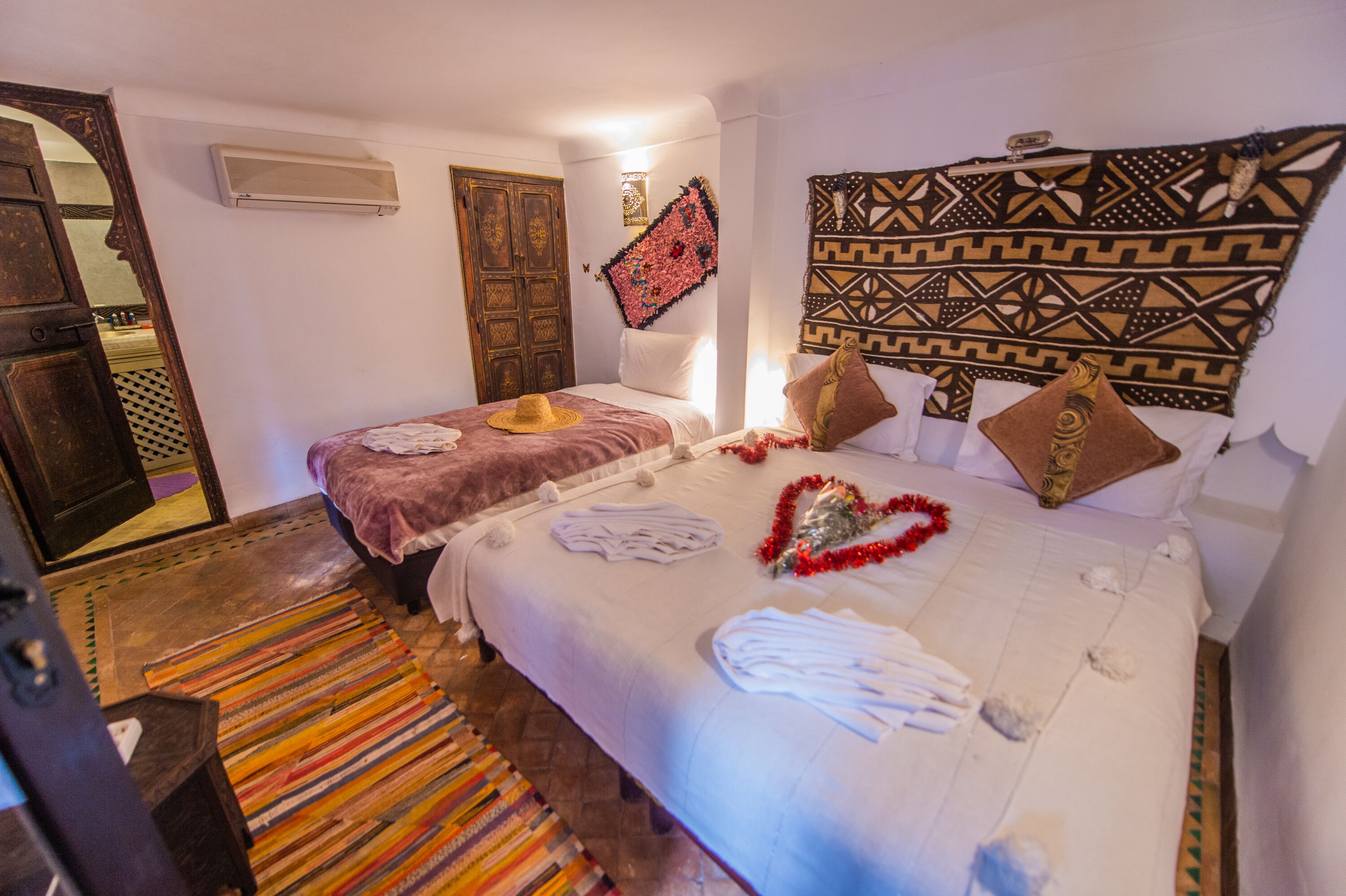 Una habitación de hotel con dos camas, un cabecero estampado, un espejo y una alfombra a rayas colorida.