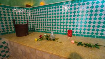 Un baño con salpicadero de azulejos a cuadros, un lavamanos y una encimera con una botella, un vaso rojo y flores.