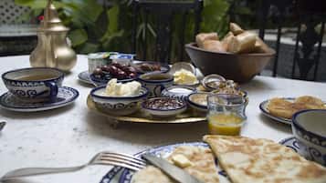 Una mesa servida con una variedad de platos, incluyendo pan, aceitunas y queso, junto con una tetera de bronce y cuencos sobre un mantel blanco.