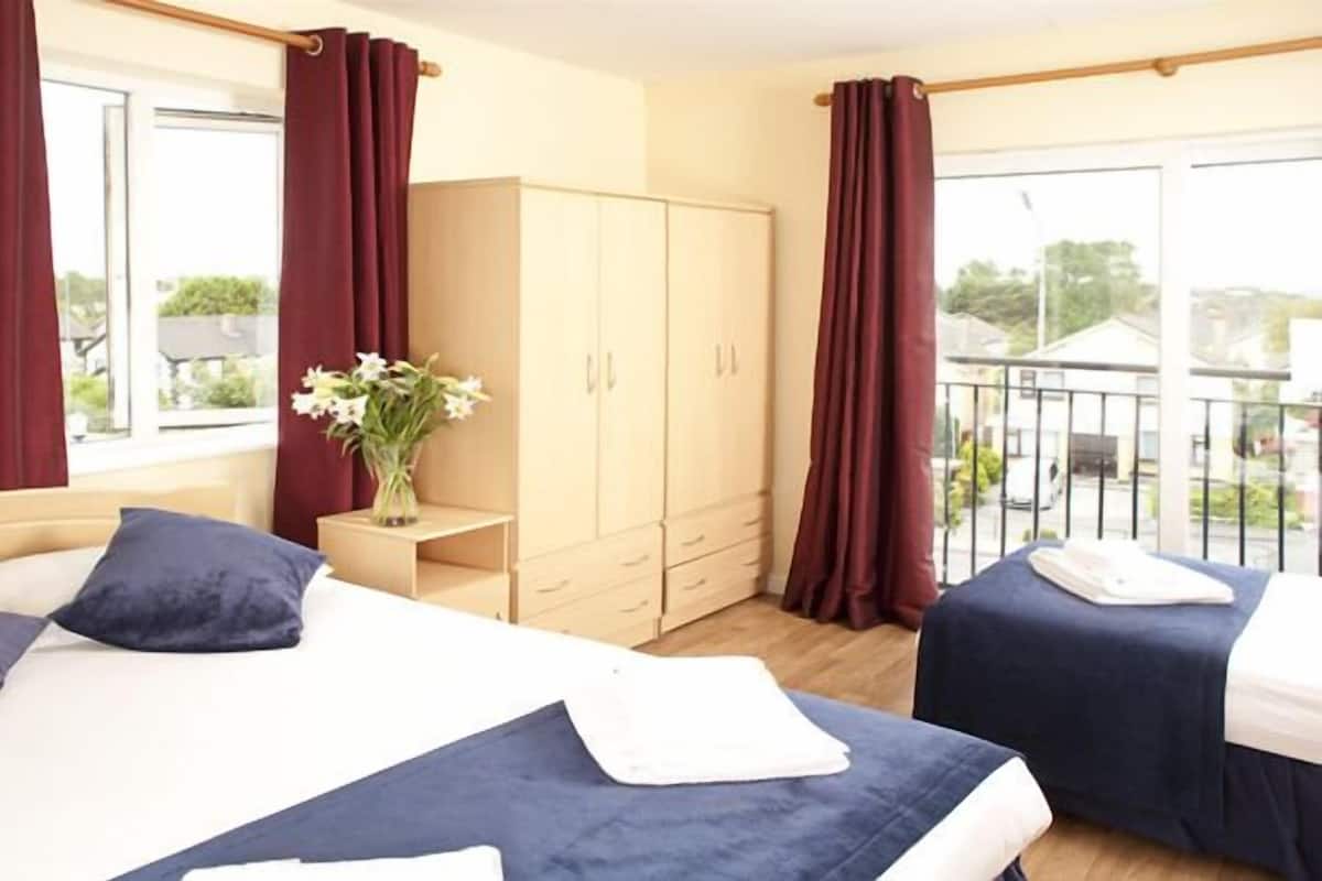 Een hotelkamer met twee bedden, een kledingkast, een klein tafeltje met een bloemenvaas en een balkon met een hekwerk.