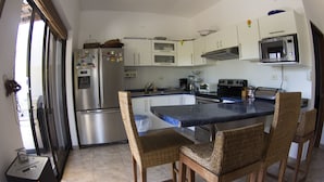 A kitchen with a stainless steel refrigerator, a microwave, and a toaster. There are wicker chairs around a central island.