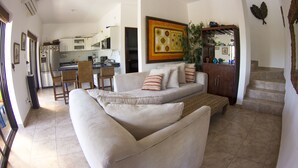 A living room with a sofa, a dining area with chairs, a kitchen in the background, and a staircase leading upstairs.
