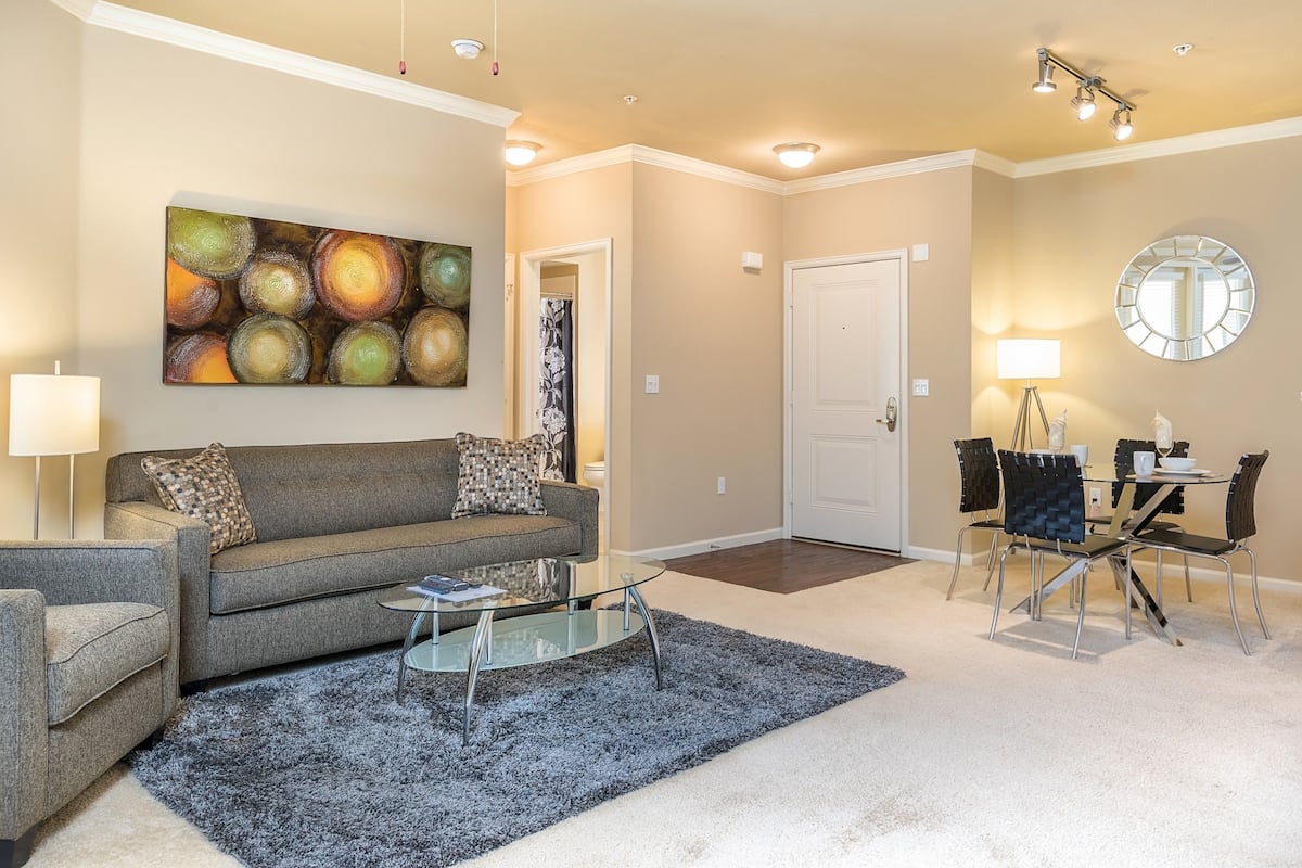A living room with a gray sofa, a glass coffee table, and a dining area with a round table and chairs.