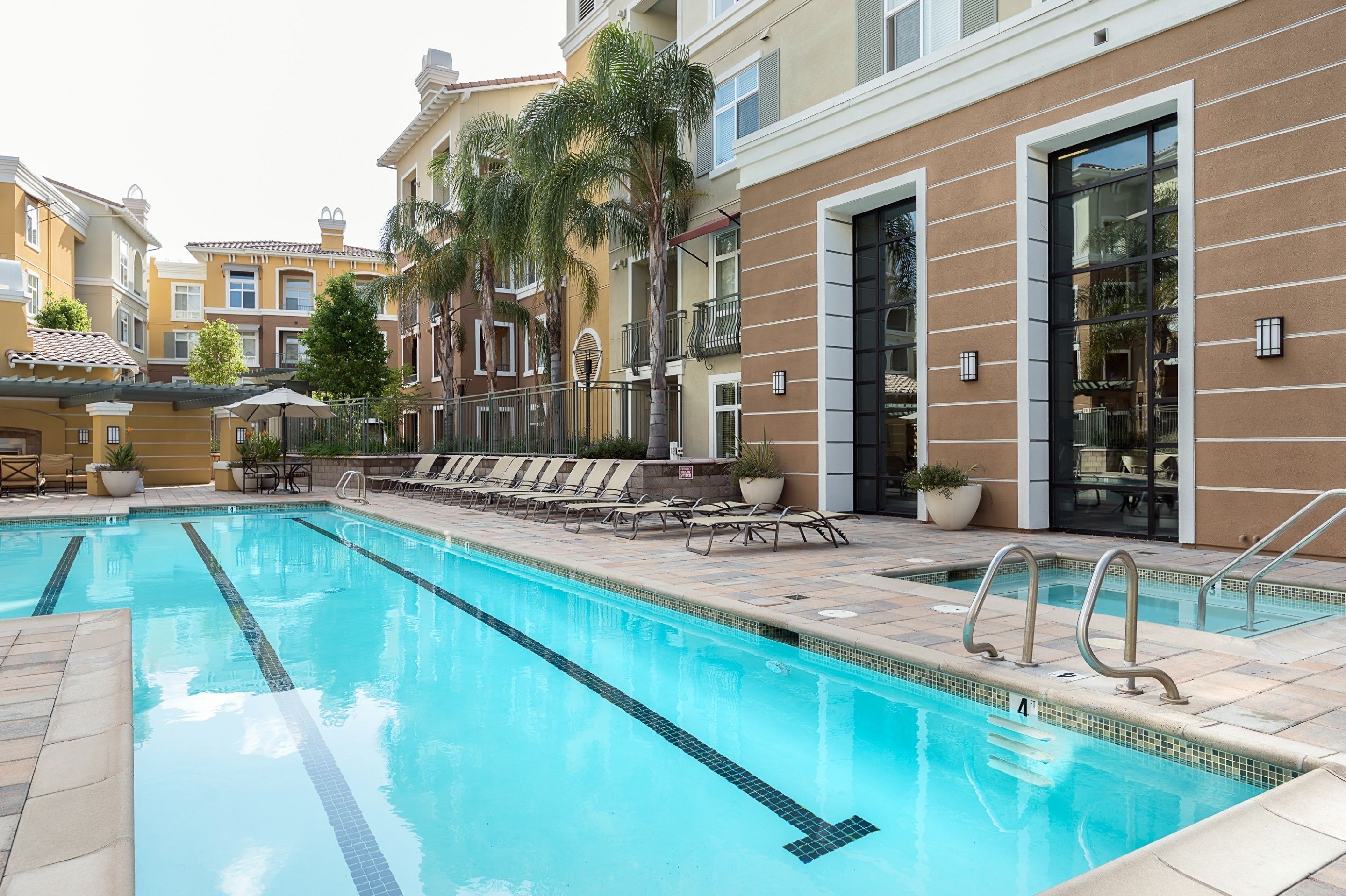 A swimming pool with lounge chairs and a building with balconies and large windows.