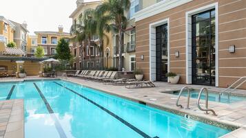 A swimming pool with lounge chairs and a building with balconies and large windows.