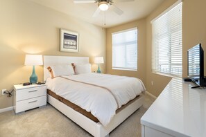 Quarto com cama, mesas de cabeceira, escrivaninha e ventilador de teto.