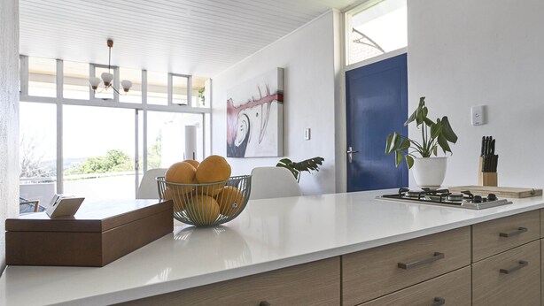A modern kitchen with a white countertop, a bowl of fruit, a laptop, and a potted plant. - House Sandrock Muckleneuk (Pretoria)