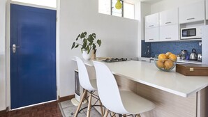A modern kitchen with white cabinets, a blue door, and a central island with chairs. - House Sandrock Muckleneuk (Pretoria)