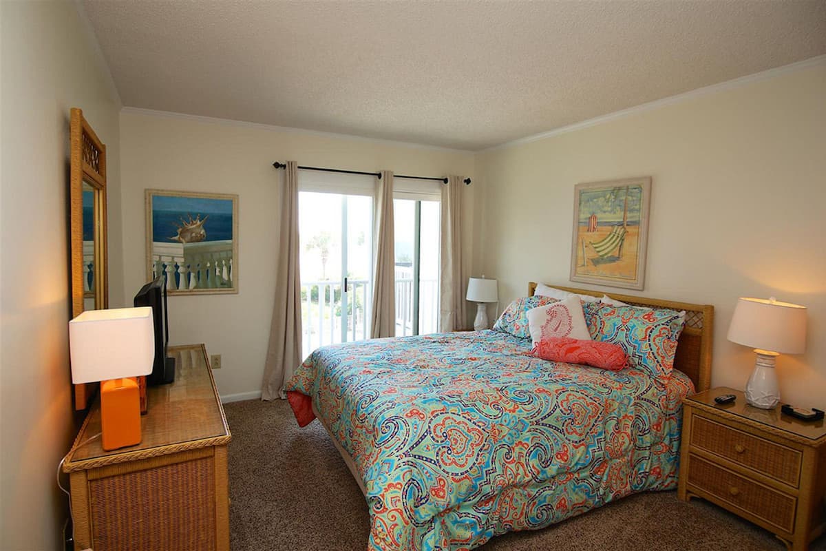 A bedroom with a bed, two bedside tables, a mirror, and a window with curtains.