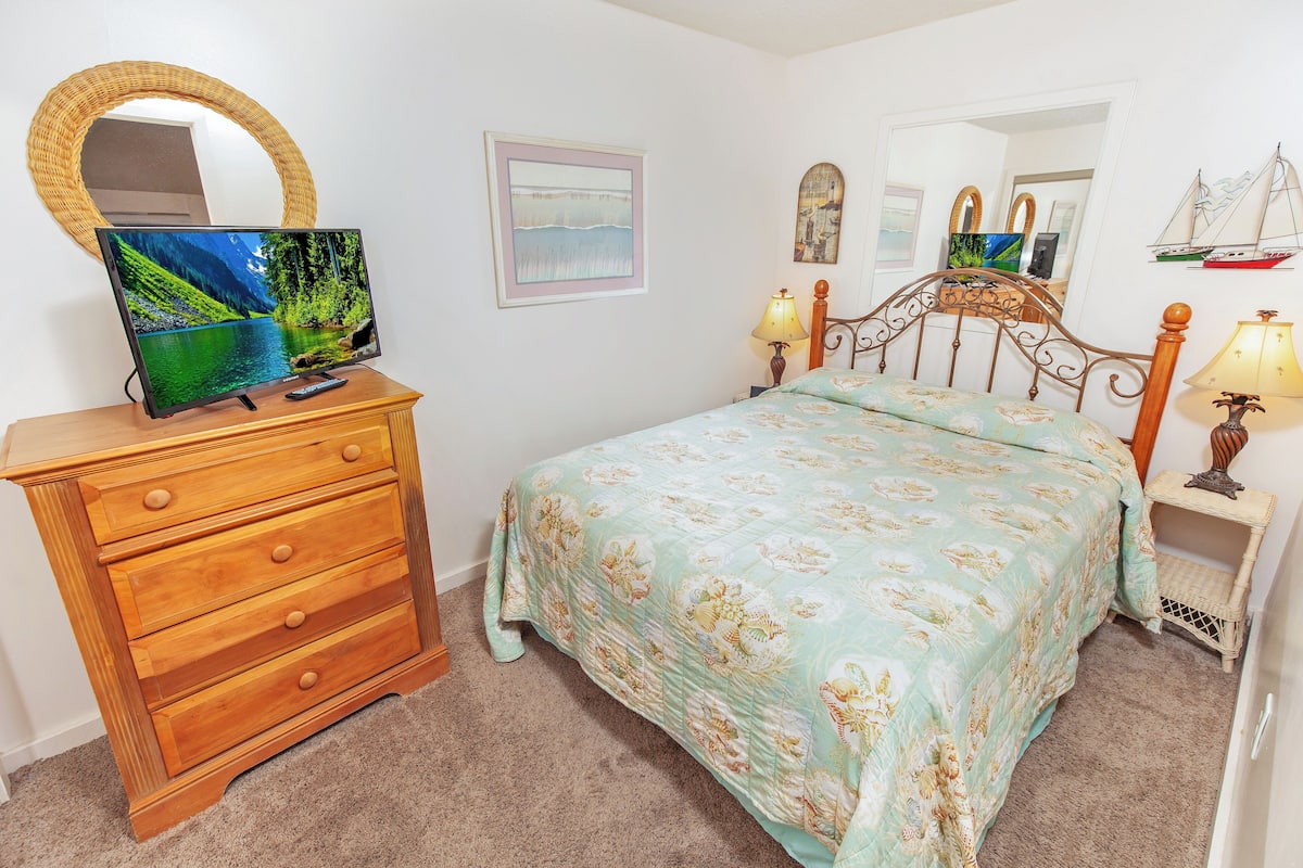A bedroom with a bed, a dresser, a TV, and a lamp.