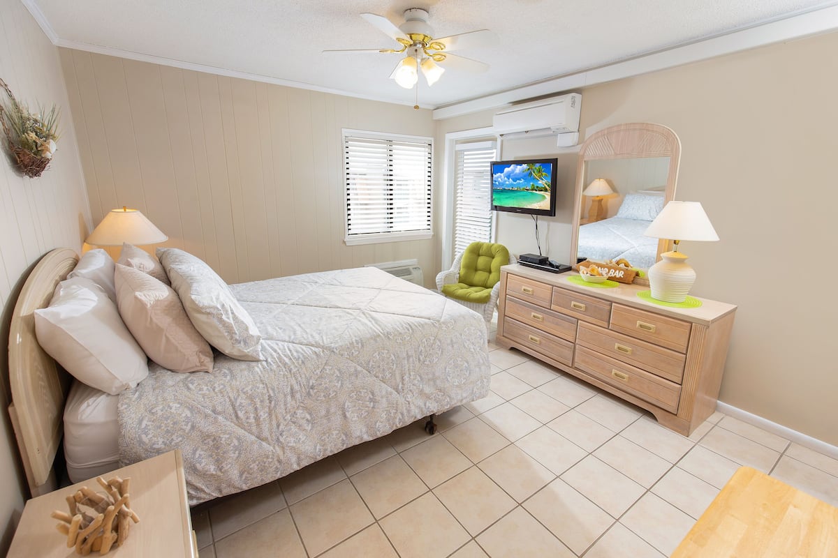 A bedroom with a bed, a dresser, a television, and a ceiling fan.