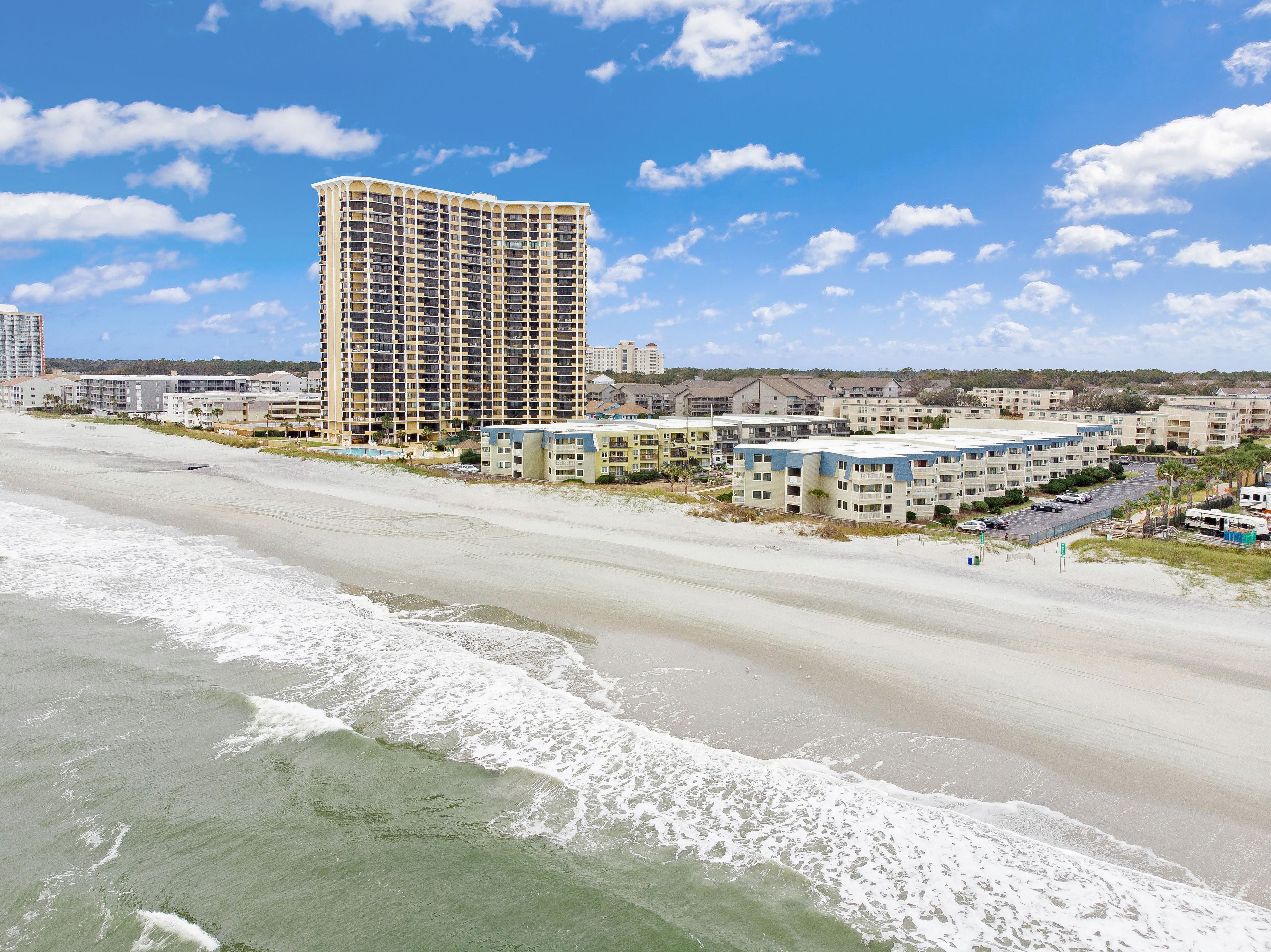 A beachfront hotel with multiple buildings, including a tall hotel and several smaller structures.